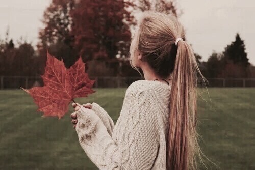 блондинка в свитере спиной не видно лица с большим кленовым листом осенью