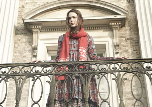 девушка с красным шарфом в клетчатом платье стоит на балконе