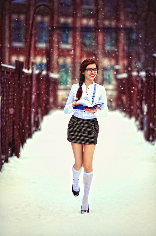 красивая школьница в очках и гольфах улыбается шагая под снегом