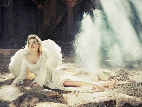 девушка с белыми крыльями в длинном платье лежит на развалинах смотря вверх в небо