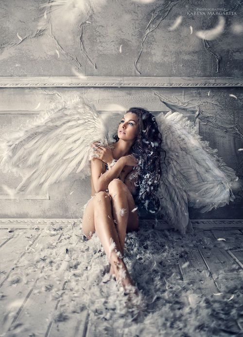 девушка сидит под стеной в перьях от крыльев ангела