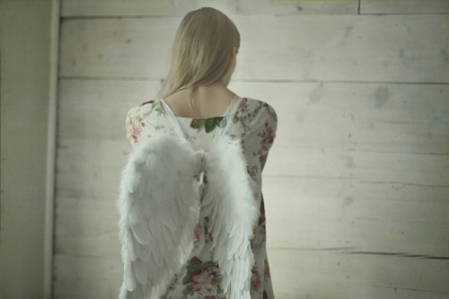 блондинка спиной в белом платье с цветочным принтом с крыльями ангела