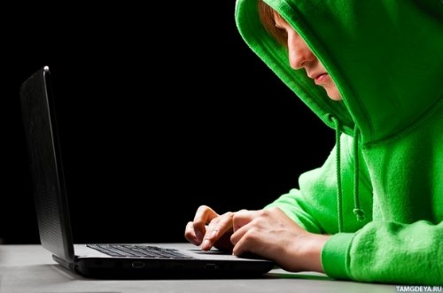 парень в зеленом капюшоне сидит за ноутбуком