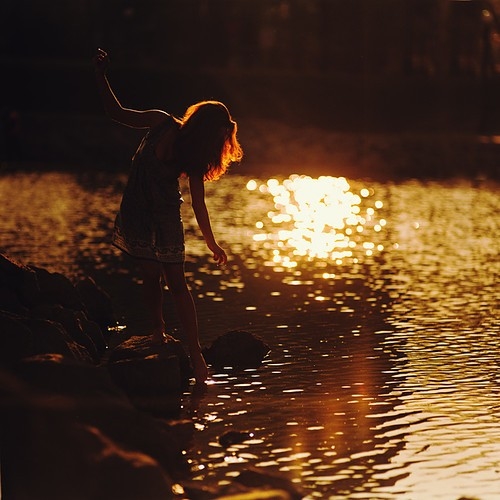 девушка в летнем сарафане пробует воду кончиком пальцев ноги