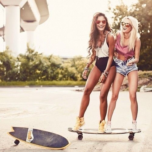 две подружки на одном скейте смеются летом