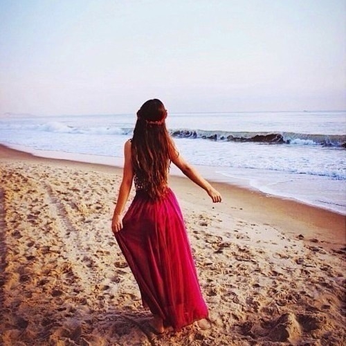 девушка с каштановыми волосами по пояс в длинном платье на берегу моря с мокрым песком