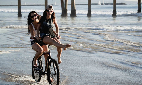 подружки катают друг друга на руле велосипеда вдоль моря летом