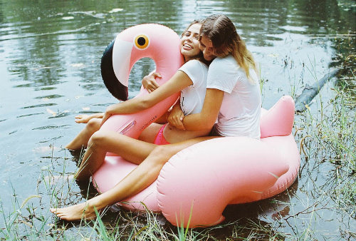 две девушки катаются на надувном розовом фламинго по реке