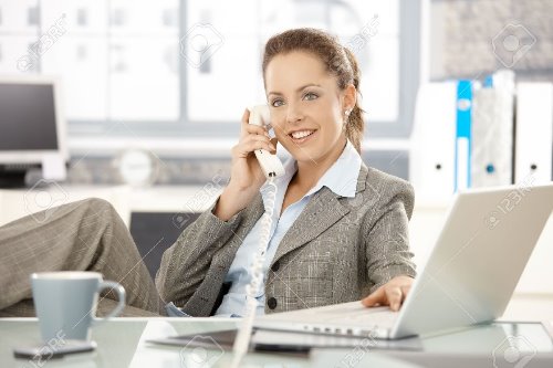 девушка в деловом костюме говорит по телефону за рабочим столом