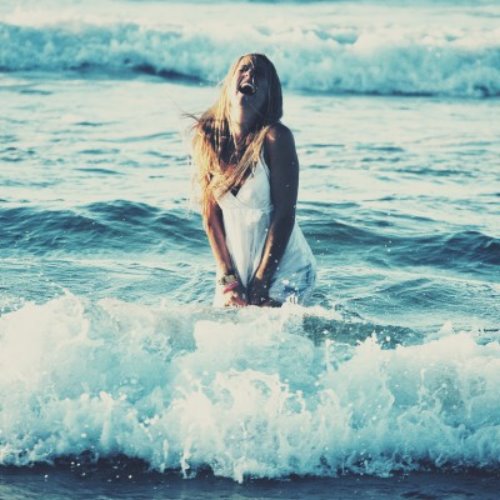 блондинка в белом платье в морских волнах смеется запрокинув голову