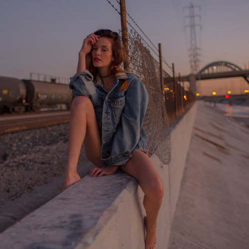 девушка в джинсовой куртке сидит на заборе в сумерки в городе