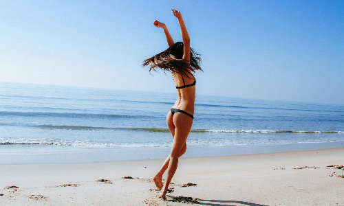 девушка в купальнике стрингах кружится на пляже