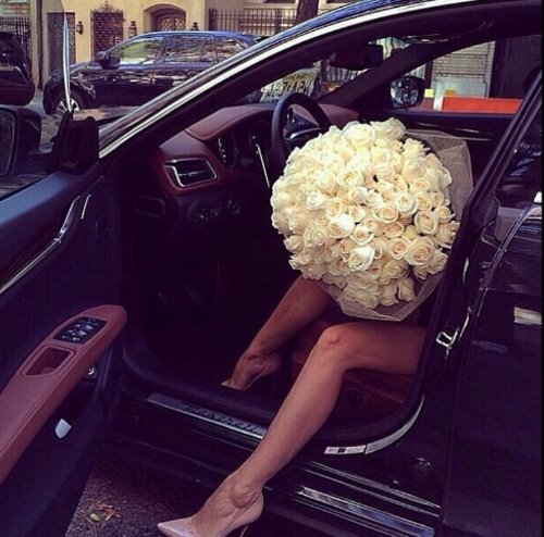 девушка выходит из автомобиля с большим белым букетом роз