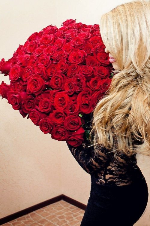 блондинка с пухлыми губами в черном платье с букетом красных роз