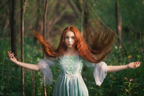 рыжая девушка подбрасывает волосы в воздух в голубом платье в лесу