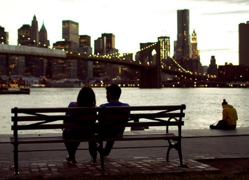 влюбленные любуются вечерним мостом сидя на скамейке спиной