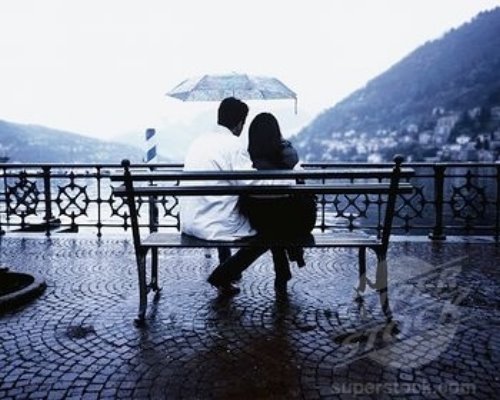 влюбленные под дождем сидят на скамейке под зонтом