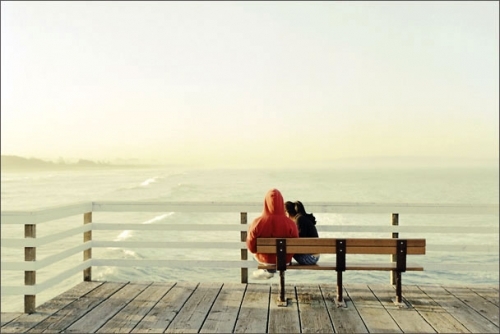 парень в капюшоне девушка сидит у него на руках на скамейке в море