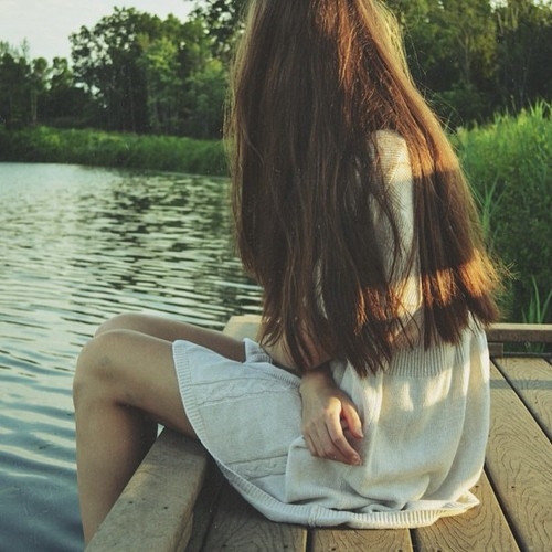 девушка с длинными ногами сидит у озера спустив ноги в воду