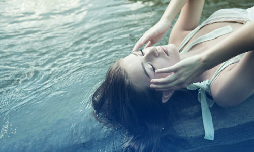 девушка мочит волосы в фонтане держа руки у висков