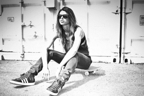 девушка в джинсах и солнцезащитных очках сидит на скейте