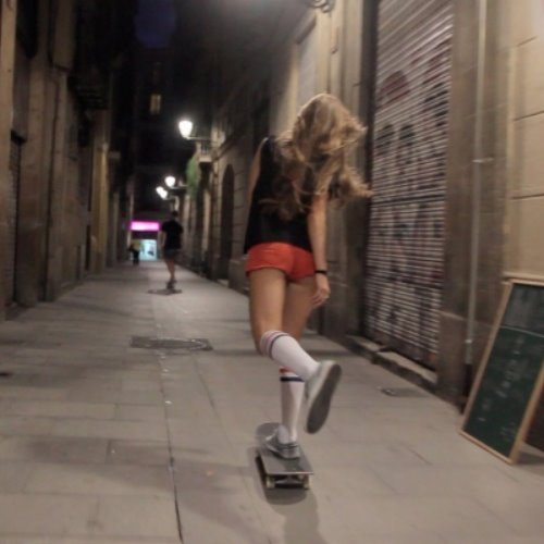 девушка в коротеньких красных шортах со спины разгоняется на скейте