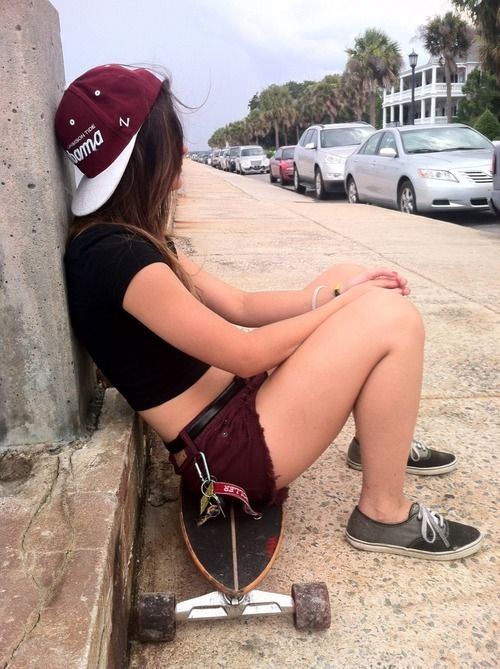девушка отдыхает под стеной на скейте возле дороги