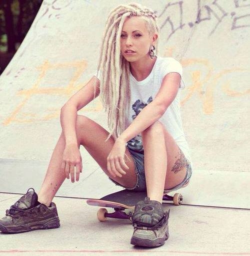 блондинка с дредами сидит на скейте в кроссовках без шнурков