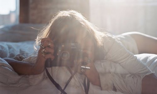 девушка с фотоаппаратом лежит на животе на кровати в лучах солнца не видно лица