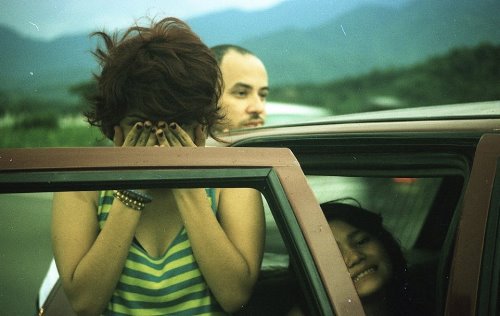 девушка в полосатой майке прикрыла лицо руками с черными ногтями возле машины