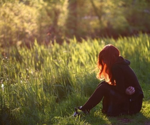 рыжая девушка сидит обняв себя за живот в траве