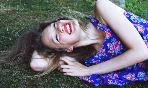 девушка в синем платье смеется лежа на траве летом