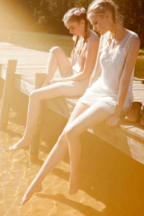 две девушки мокают ноги в пруд принимая солнечные ванны