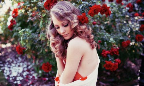 очень красивая девушка с локонами среди цветущих роз