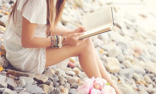 девушка в белом платье читает на каменном берегу