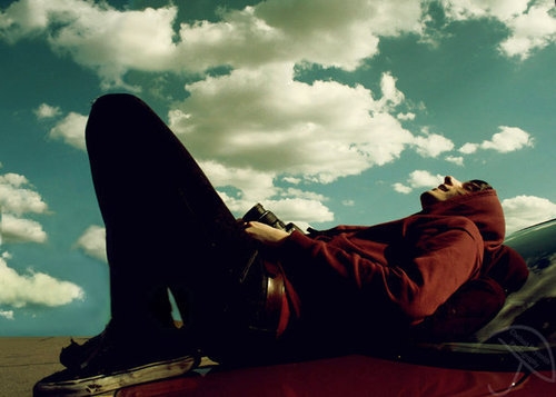 парень лежит на капоте и любуется облаками