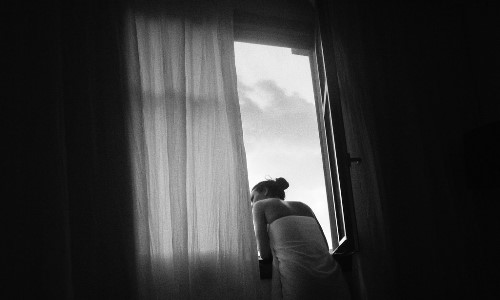 черно белое фото девушки со спины обматанной в белое полотенце выглядывающей в окно