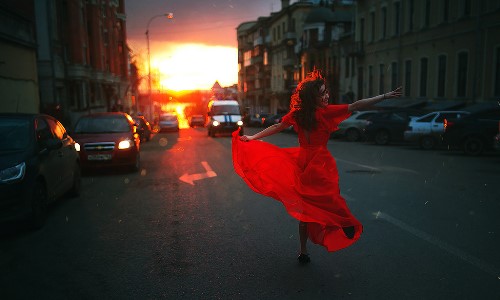 девушка в красном платье танцует на проезжей части в лучах солнца
