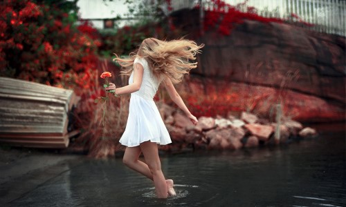 девушка в белом платье танцует в воде держа в руке розу, волосы развиваются в танце
