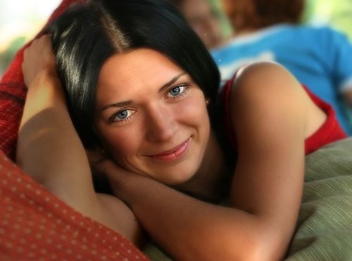 девушка с черными волосами и синими глазами в красной майке лежит и улыбается