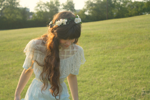 милая девушка в венке из белых цветов в платье идет по траве длинные волосы