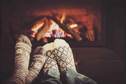 мужские и женские ножки в теплых носочках с принтом греются у камина, новогоднее настроение