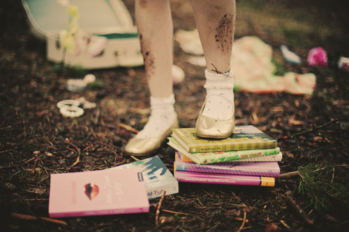 грязные ножки девочки топчут стопку книг и тетрадей на земле