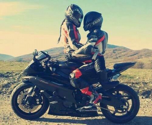 Влюбленная пара в мотоциклетной одежде обнимаются на мотоцикле.