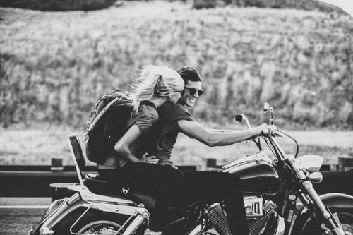 Пара в солнцезащитных очках катается на мотоцикле, ветер раздувает светлые волосы девушки с рюкзаком.