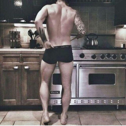 мужчина в плавках со спины готовит завтрак на плите на кухне