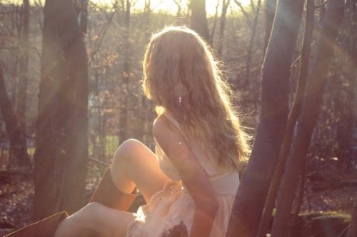Блондинка в осеннем лесу в солнечных лучах. Одета в белое платье и высокие коричневые сапоги. Вид со спины.
