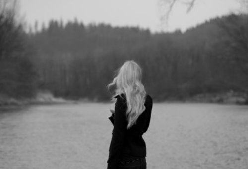 Блондинка в черном платье у реки спиной, мрачная депрессивная фотография