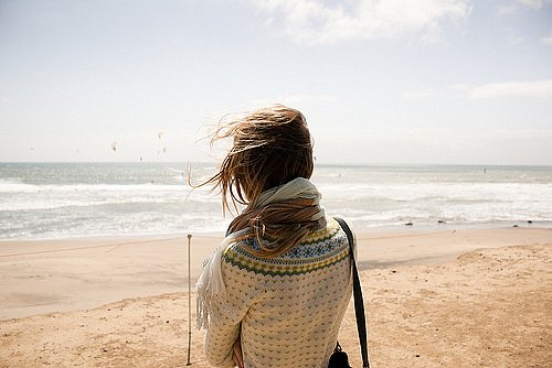Девушка спиной под ветром у моря в свитере