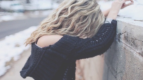 Блондинка с волнистыми волосами в вязаном свитере у стены на улице без лица